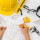 hand-over-construction-plans-with-yellow-helmet-and-drawing-tool (1)
